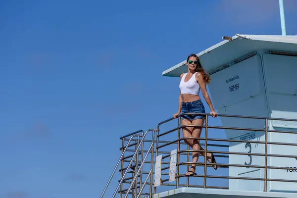 stock image Breathtaking woman basks in beach bliss, near a pier, under clear blue skies, embracing the serenity of a perfect day by the sea