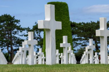 Normandiya Amerikan Mezarlığı 'ndaki sonsuz beyaz haç sıralarının arasında dururken tarihin ağırlığı aşikardır. Kasvetli sessizlik sadece esintiyle kırılır, yapılan fedakarlıkların dokunaklı bir hatırlatıcısı..