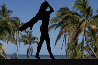 Büyüleyici Karayipler 'de, göz alıcı bir kadın çarpıcı bir kumsalda poz verir, silueti canlı mavi gökyüzü ile süslenir, zamansız güzelliği ve kıyı cazibesini somutlaştırır..