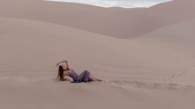 Zarif model kum tepelerindeki doğanın güzelliğini kucaklıyor, engin, doğal ihtişamın arkaplanına karşı zarafeti simgeliyor.