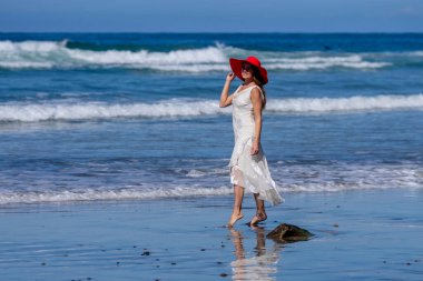 Nefes kesen kadın kumsaldaki mutluluğun tadını çıkarıyor, bir rıhtımın yanında, açık mavi gökyüzünün altında, deniz kıyısında mükemmel bir günün dinginliğini kucaklıyor.