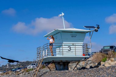 Nefes kesen kadın kumsaldaki mutluluğun tadını çıkarıyor, bir rıhtımın yanında, açık mavi gökyüzünün altında, deniz kıyısında mükemmel bir günün dinginliğini kucaklıyor.