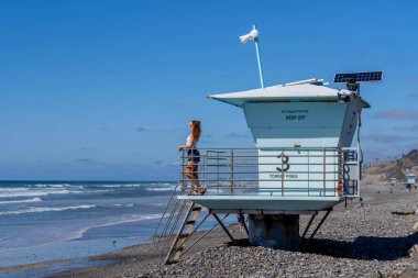Nefes kesen kadın kumsaldaki mutluluğun tadını çıkarıyor, bir rıhtımın yanında, açık mavi gökyüzünün altında, deniz kıyısında mükemmel bir günün dinginliğini kucaklıyor.