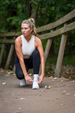 Güzel, sarışın bir model, şık idman kıyafetleri giymiş, yoğun bir egzersizden sonra hak ettiği molayı alıyor. Temiz havada rahatlar, kendine güven ve canlılık saçar..