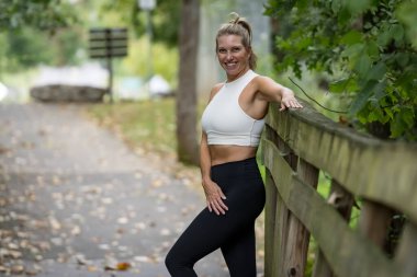 Güzel, sarışın bir model, şık idman kıyafetleri giymiş, yoğun bir egzersizden sonra hak ettiği molayı alıyor. Temiz havada rahatlar, kendine güven ve canlılık saçar..