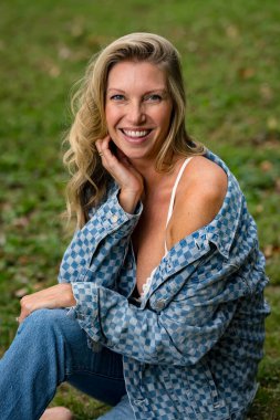 Güzel bir sarışın manken yaz sonu güneşinin tadını çıkarıyor. Bereketli yeşillik ve yumuşak güneş ışığıyla çevrili, o, sıcaklığı ve zarafeti serin, altın ışıkta yayar..