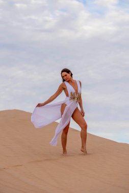 Zarif model kum tepelerindeki doğanın güzelliğini kucaklıyor, engin, doğal ihtişamın arkaplanına karşı zarafeti simgeliyor.