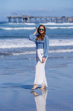 Nefes kesen kadın kumsaldaki mutluluğun tadını çıkarıyor, bir rıhtımın yanında, açık mavi gökyüzünün altında, deniz kıyısında mükemmel bir günün dinginliğini kucaklıyor.