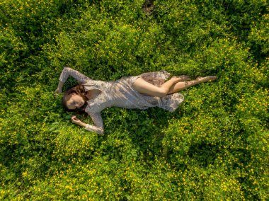Muhteşem, genç, esmer bir iç çamaşırı mankeni, bahar gününün dinginliği içinde uzun yeşil çimenlerin arasında rahatlar. Evinin güzelliğini ve sükunetini kucaklayarak huzur saçar..