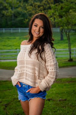 Güzel, esmer, güneyli bir kadın kameraya şık bir kesim kot pantolon ve rahat bir kazakla poz veriyor. İlkbahar gibi bir günün güzelliğinin tadını çıkarırken aynı zamanda cazibesini de yansıtıyor..