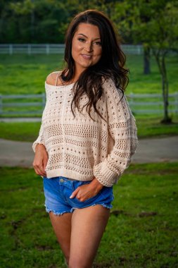 Güzel, esmer, güneyli bir kadın kameraya şık bir kesim kot pantolon ve rahat bir kazakla poz veriyor. İlkbahar gibi bir günün güzelliğinin tadını çıkarırken aynı zamanda cazibesini de yansıtıyor..