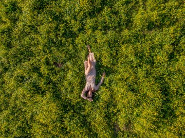 Muhteşem, genç, esmer bir iç çamaşırı mankeni, bahar gününün dinginliği içinde uzun yeşil çimenlerin arasında rahatlar. Evinin güzelliğini ve sükunetini kucaklayarak huzur saçar..