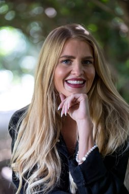 Işıl ışıl sarışın bir kadın kıtır sonbahar havasının tadını çıkarıyor. Gözleri altın güneş ışığında parıldıyor. Sıcak parıltı, onun genç tenini ön plana çıkarıyor. Açık havada güzellik ve huzur dolu mükemmel bir an yaratıyor..