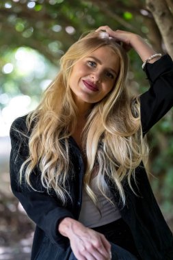 Işıl ışıl sarışın bir kadın kıtır sonbahar havasının tadını çıkarıyor. Gözleri altın güneş ışığında parıldıyor. Sıcak parıltı, onun genç tenini ön plana çıkarıyor. Açık havada güzellik ve huzur dolu mükemmel bir an yaratıyor..