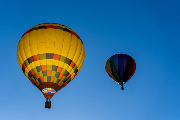 Vibrant air balloons of all shapes and colors soar into the clear blue sky, filling the air with excitement during a crisp autumn balloon fest. The scene is breathtaking against the season's beauty.
