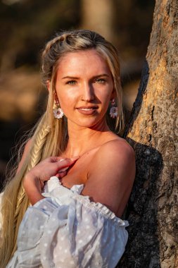 Göz kamaştırıcı genç bir kadın bir dere kenarında yürüyor, beyaz bahar elbisesi rüzgarda zarif bir şekilde sallanıyor. Etrafı yemyeşil ormanlarla çevrili mükemmel bir bahar gününün huzur ve güzelliğinin tadını çıkarıyor..