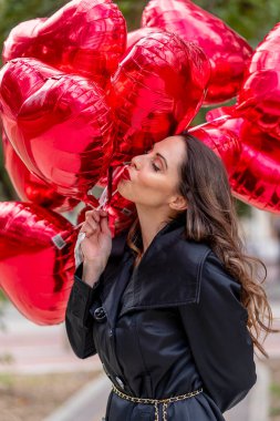Güzel bir esmer, bir düzine kırmızı kalp şeklinde balon tutarak hareketli bir şehir caddesinde yürüyor. Sevgilisiyle buluşmak için Sevgililer Günü kaçamağına giderken gülümsemesi heyecanını yansıtıyor..