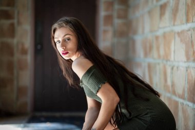 Çekici genç bir esmer, dalgalı beyaz bir bahar elbisesi içinde, saçları dalgalar halinde dalgalanırken dışarıda poz veriyor. Gülümsüyor, uzun ve sert bir kışın ardından baharın yumuşak sıcağında güneşleniyor..