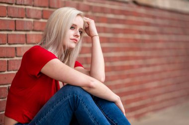 Güzel sarışın bir kadın, şık bahar kıyafetlerini göstererek kameraya neşe içinde poz veriyor. Parlak bir gülümseme ve neşeli tavırlarıyla yaklaşan muhteşem havayı kucaklayarak mutluluk saçıyor..