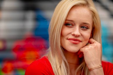 Güzel sarışın bir kadın, şık bahar kıyafetlerini göstererek kameraya neşe içinde poz veriyor. Parlak bir gülümseme ve neşeli tavırlarıyla yaklaşan muhteşem havayı kucaklayarak mutluluk saçıyor..