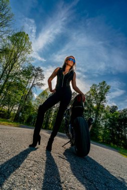 A stunning woman strikes a confident pose beside her high-performance motorcycle. With a fierce gaze and poised stance, she radiates power and passion, embodying the spirit of the open road. clipart