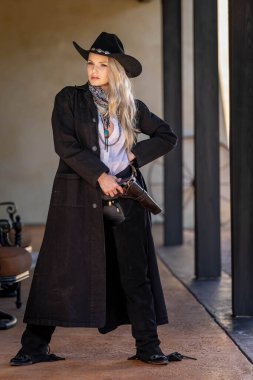 Klasik kovboy kıyafetli, kendine güvenen, güzel, sarışın bir kadın uzun boylu, kalçasında bir tabanca ve omzunda bir tüfekle poz veriyor. Gülüşü enerji ve korkusuz cazibe saçıyor..