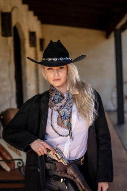 Klasik kovboy kıyafetli, kendine güvenen, güzel, sarışın bir kadın uzun boylu, kalçasında bir tabanca ve omzunda bir tüfekle poz veriyor. Gülüşü enerji ve korkusuz cazibe saçıyor..