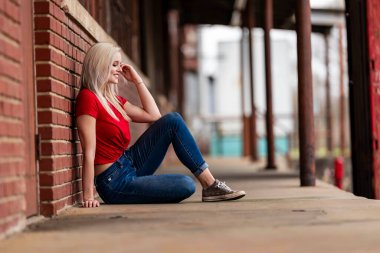 Güzel sarışın bir kadın, şık bahar kıyafetlerini göstererek kameraya neşe içinde poz veriyor. Parlak bir gülümseme ve neşeli tavırlarıyla yaklaşan muhteşem havayı kucaklayarak mutluluk saçıyor..