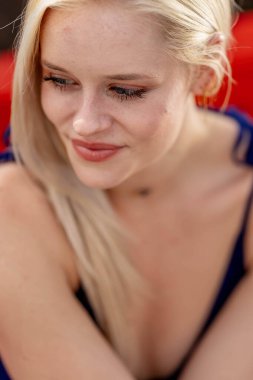 Güzel sarışın bir kadın, şık bahar kıyafetlerini göstererek kameraya neşe içinde poz veriyor. Parlak bir gülümseme ve neşeli tavırlarıyla yaklaşan muhteşem havayı kucaklayarak mutluluk saçıyor..