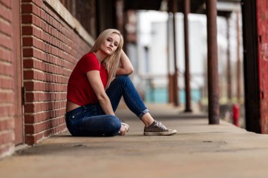 Güzel sarışın bir kadın, şık bahar kıyafetlerini göstererek kameraya neşe içinde poz veriyor. Parlak bir gülümseme ve neşeli tavırlarıyla yaklaşan muhteşem havayı kucaklayarak mutluluk saçıyor..