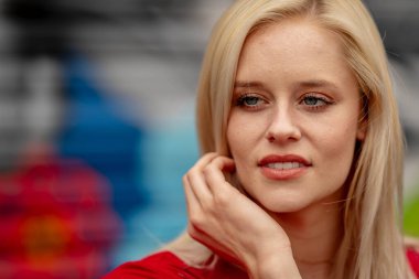 Güzel sarışın bir kadın, şık bahar kıyafetlerini göstererek kameraya neşe içinde poz veriyor. Parlak bir gülümseme ve neşeli tavırlarıyla yaklaşan muhteşem havayı kucaklayarak mutluluk saçıyor..