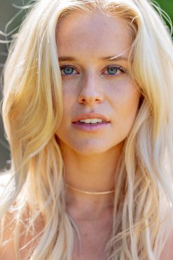 Güzel bir sarışın kadın taze, bahar gibi havanın tadını çıkarıyor, açık havada, yemyeşil bir alanda, canlı çiçeklerle dolu. Etrafında çiçek açan güzelliğiyle neşe ve uyum saçar.