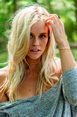 Büyüleyici bir sarışın, narin iç çamaşırlarıyla yemyeşil tarlalar ve çiçek açan çiçeklerin arasında poz vererek baharın sıcağında güneşleniyor. Doğanın güzelliğini kusursuz bir şekilde kucaklayan neşe ve zarafet saçıyor..