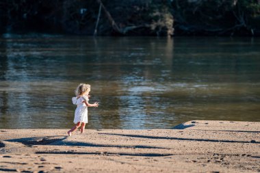 Güzel, genç bir kız, neşeyle, ışıl ışıl bir derenin kenarında oynuyor. Gülüşü, suyun yumuşak akışına uyum sağlıyor. Ilık bahar güneşinde dönüyor, doğanın güzelliğini kucaklıyor..