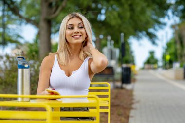Genç bir kadın, güzel bir bahar gününde elinde telefonla tuhaf kasabasında geziniyor. Çiçekler ve ılık güneş ışığıyla çevrili halde, teknolojiyi sakin çevresinin cazibesiyle harmanlayarak bağlı kalıyor.