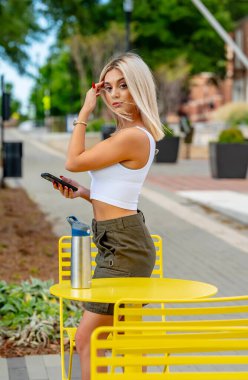 Genç bir kadın, güzel bir bahar gününde elinde telefonla tuhaf kasabasında geziniyor. Çiçekler ve ılık güneş ışığıyla çevrili halde, teknolojiyi sakin çevresinin cazibesiyle harmanlayarak bağlı kalıyor.