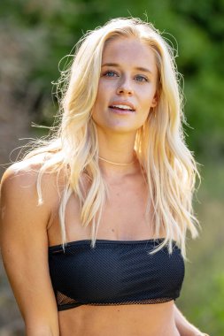 Büyüleyici bir sarışın, narin iç çamaşırlarıyla yemyeşil tarlalar ve çiçek açan çiçeklerin arasında poz vererek baharın sıcağında güneşleniyor. Doğanın güzelliğini kusursuz bir şekilde kucaklayan neşe ve zarafet saçıyor..