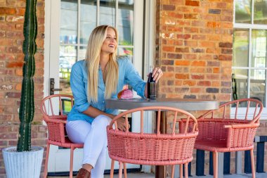 Parlak, genç, şık giyinmiş, pastanın tadını çıkaran ve açık hava alışveriş merkezinde gazoz yudumlayan bir sarışın. O canlı atmosferden ve hafif açık hava esintisinden zevk alırken güneş sıcacık bir parıltı saçar..