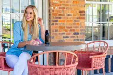 Parlak, genç, şık giyinmiş, pastanın tadını çıkaran ve açık hava alışveriş merkezinde gazoz yudumlayan bir sarışın. O canlı atmosferden ve hafif açık hava esintisinden zevk alırken güneş sıcacık bir parıltı saçar..