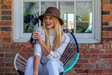 Şık giyinmiş, göz kamaştırıcı genç bir sarışın açık hava alışveriş merkezinde gazoz içiyor. Güneş onu sıcağa boğuyor. O, canlı ve açık havada esen enerjiyi ve rahatlatıcı esintiyi içine çekerken..