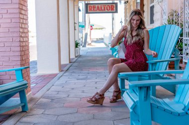 Genç, güzel, sarışın bir kadın kasabayı geziyor, büyüleyici yerel dükkanlara göz atıyor. Neşeli manzaranın, sıcak güneşin ve mükemmel havanın tadını çıkarıyor. Rahat ve neşeli bir günün tadını çıkarıyor.