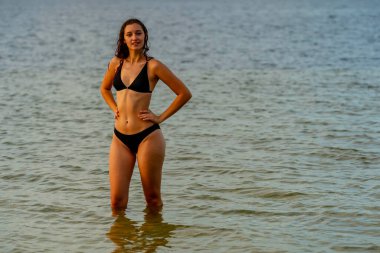 Çekici bir kadın plajda kıvrımlarını gösteren bir bikiniyle rahatlar. Soğuk suyun ve güneşin altında güneşlenmenin tadını çıkarıyor. Güneş ışınlarıyla sırılsıklam olurken altın bronzlaşmayı da..