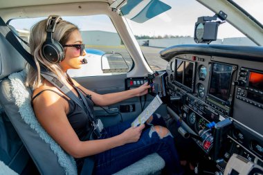 Genç bir kadın pilot uçuş öncesi kontrollerini titizlikle gerçekleştiriyor. Hava aracının yanında, açık mavi gökyüzünün altında, kusursuz bir uçuş gününde hassasiyet ve tutkuyu somutlaştırıyor..