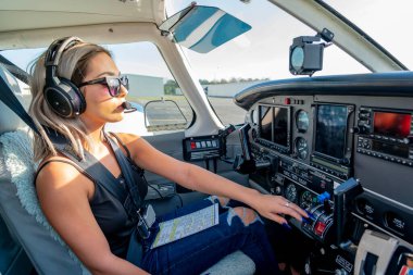 Genç bir kadın pilot uçuş öncesi kontrollerini titizlikle gerçekleştiriyor. Hava aracının yanında, açık mavi gökyüzünün altında, kusursuz bir uçuş gününde hassasiyet ve tutkuyu somutlaştırıyor..