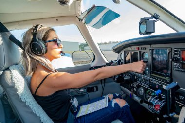 Genç bir kadın pilot uçuş öncesi kontrollerini titizlikle gerçekleştiriyor. Hava aracının yanında, açık mavi gökyüzünün altında, kusursuz bir uçuş gününde hassasiyet ve tutkuyu somutlaştırıyor..