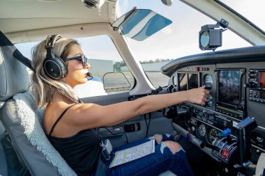 A young woman pilot diligently performs pre-flight checks beside her general aviation aircraft, under clear blue skies, embodying precision and passion on a perfect flying day. clipart