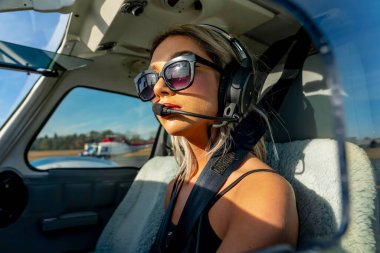 Genç bir kadın pilot uçuş öncesi kontrollerini titizlikle gerçekleştiriyor. Hava aracının yanında, açık mavi gökyüzünün altında, kusursuz bir uçuş gününde hassasiyet ve tutkuyu somutlaştırıyor..
