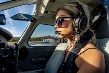 Genç bir kadın pilot uçuş öncesi kontrollerini titizlikle gerçekleştiriyor. Hava aracının yanında, açık mavi gökyüzünün altında, kusursuz bir uçuş gününde hassasiyet ve tutkuyu somutlaştırıyor..