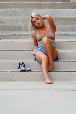 Göz kamaştırıcı sarışın bir kadın, sıcacık gülümseyerek bahar havasının ve büyüleyici manzaranın tadını çıkarırken küçük bir kasabada geziniyor..