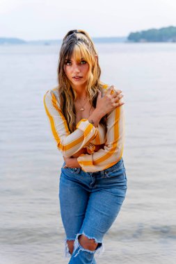 Işıl ışıl, koyu kahverengi ve karamel renkli iki tonlu saçları olan Meksikalı genç bir Amerikalı kadın sıcak bir şekilde gülümsüyor. Berrak bir göl kenarında güneşli bir yaz gününün tadını çıkarıyor. Etrafı yemyeşil ve ışıldayan suyla çevrili..